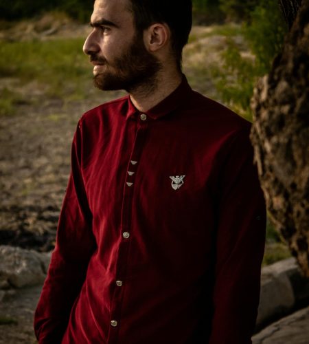 Fashionable man in a red shirt standing outdoors, gazing into the distance during twilight.